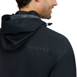 LeMieux AW26 Mens Waterproof Lightweight Jacket Varient Black. Close-up back view of a man wearing a dark navy hooded jacket with the brand name 'LEMIEUX' printed on the upper back, against a plain white background.