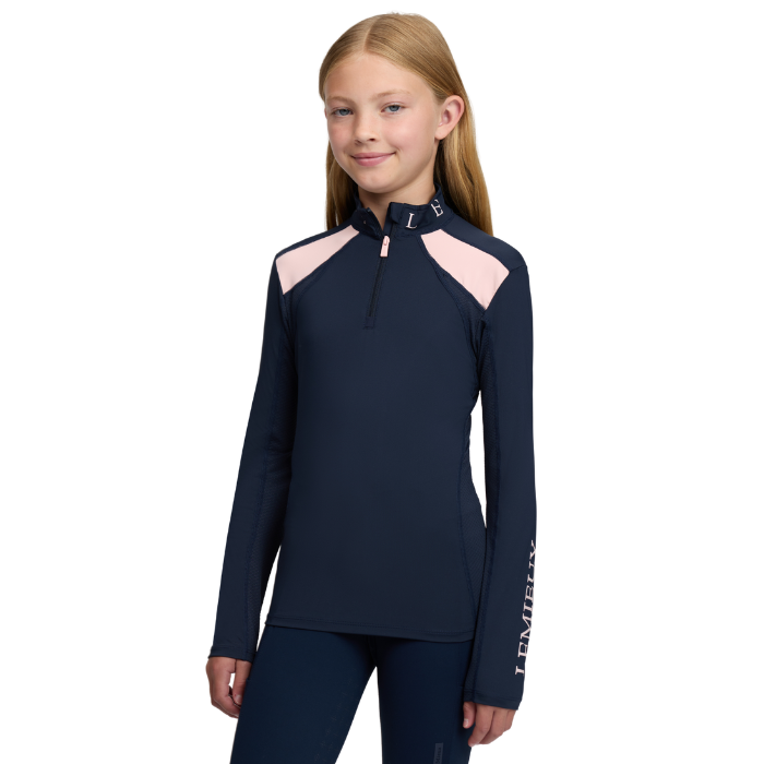 LeMieux AW26 Young Rider Mia Mesh Base Layer Varient Navy. A young girl modeling a navy blue long-sleeve athletic quarter-zip top with light pink shoulder panels and white vertical branding on the sleeve, set against a plain white background.
