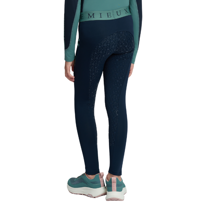 LeMieux AW26 Mini Pull Ons Varient Navy/Aloe. A person shown from the back wearing dark navy leggings with a subtle tonal pattern on the upper thighs, a teal and navy long-sleeve top, and teal sneakers against a plain white background.