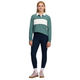 LeMieux AW26 Young Rider Riley Rugby Shirt Varient Aloe. A young woman modeling a long-sleeve collared rugby shirt in sage green and cream, paired with navy blue leggings and pink sneakers, against a plain white background.