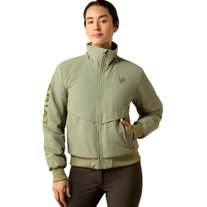 Ariat Women's Stable 2.0 Insulated Jacket Varient Oil Green. Woman wearing a olive bomber coat and black trousers on a white background. 
