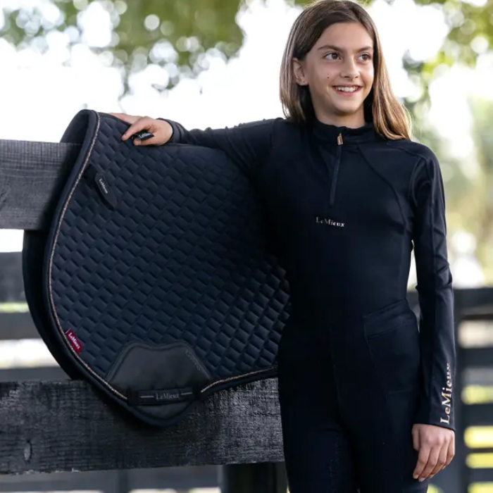 Woman in equestrian attire holding a black quilted saddle pad with 'LeMieux' branding.