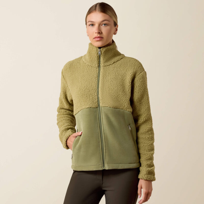 Ariat Ladies Laviolette Full Zip Jacket Variant Oil Green. A woman modeling a fleece zip-up jacket with a colorblock design, featuring a textured khaki upper section and a solid olive green lower panel, set against a plain beige background.