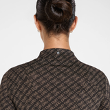 Back view of a woman wearing a dark brown collared shirt with a repeating beige geometric monogram pattern, set against a plain light gray background.