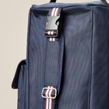 Close-up of a navy blue bag strap with red, white, and navy striped webbing and black plastic buckles, set against a plain beige background.