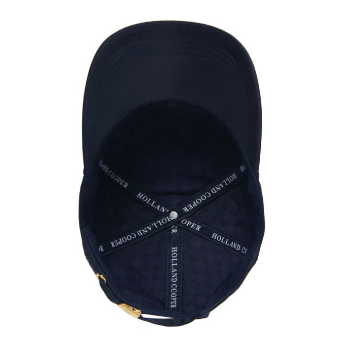 A navy blue baseball cap shown from the inside, featuring a dark navy fabric interior with white embroidered text reading 'HOLLAND COOPER' on the adjustable strap and a small gold metal adjustment slider at the bottom.