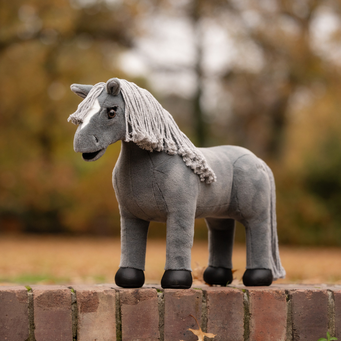 LeMieux AW26 Toy Pony Variant Colour Smokey. A plush toy pony, grey colour with grey wool mane and black feet on faded garden background.