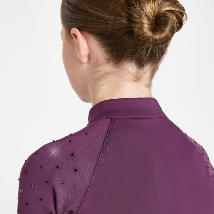 Back view of a woman wearing a purple athletic top with small black embellishments on the shoulders, against a light gray studio background.