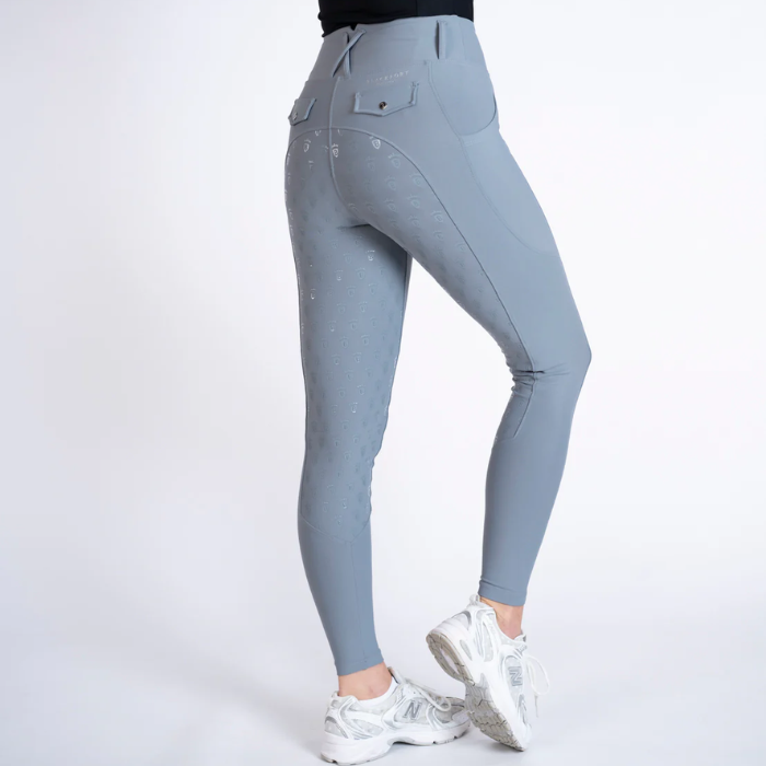 A person shown from the waist down wearing fitted high-waisted leggings in a light cool gray-blue color, with white sneakers, against a plain light gray studio background.