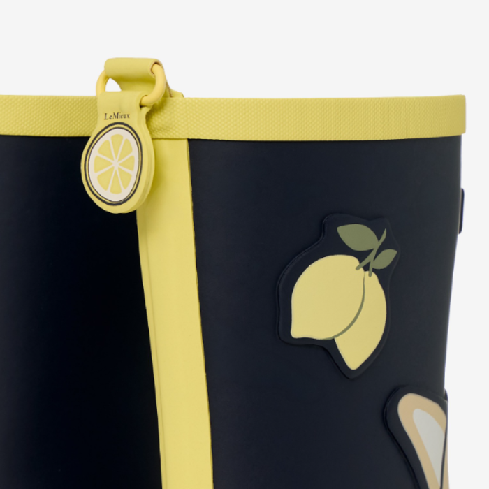 LeMieux AW26 Splash Welly Varient Lemon. Close-up of a black boot with a bright yellow trim, a yellow vertical stripe, and a raised lemon graphic on the side. A matching yellow pull tab with a lemon illustration and the word 'LeMieux' is visible near the top.