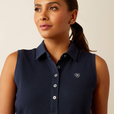 Woman wearing a navy sleeveless polo shirt with Ariat logo on a beige background