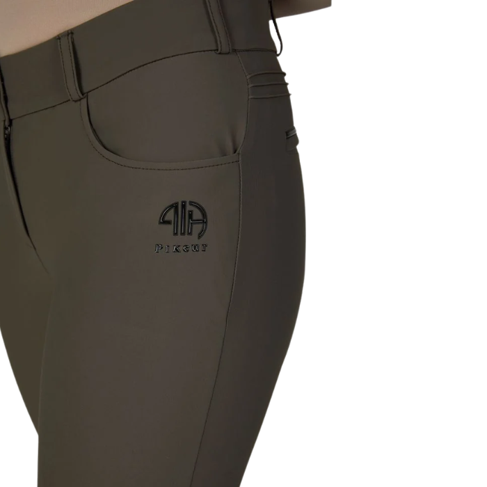Pikeur AW26 Ceelina Matrixgriptex Breeches Variant Deep Khaki. Close-up of a person wearing dark olive green riding breeches, showing the side pocket with a black embroidered logo.