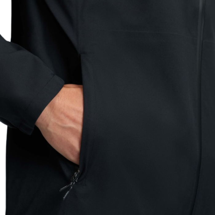 LeMieux AW26 Mens Waterproof Lightweight Jacket Varient Black. Close-up of a person wearing a black jacket, showing a hand reaching into a side pocket.