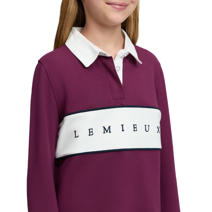 LeMieux AW26 Young Rider Riley Rugby Shirt Varient Blackberry. A close-up of a child wearing a long-sleeve rugby-style shirt in deep burgundy with a white collar, a wide white chest stripe, and the word 'LEMIEUX' printed across the front. 