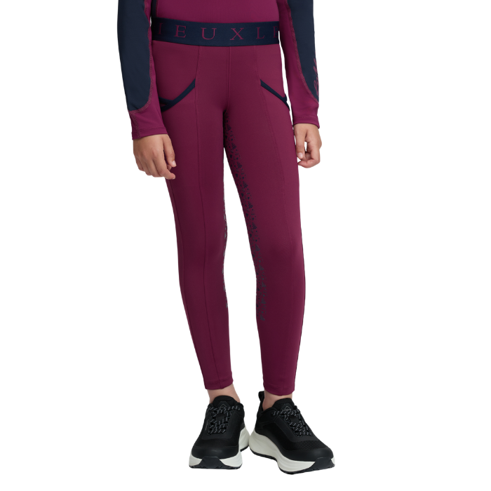 LeMieux AW26 Mini Pull Ons Varient Blackberry. A model wearing a pair of dark magenta athletic leggings with dark navy blue side panels and a matching waistband with 'LeMieux' branding, paired with black athletic shoes against a white background.