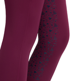 LeMieux AW26 Mini Pull Ons Varient Blackberry. Close-up of a person's leg wearing leggings in a deep berry purple, featuring a dark teal geometric pattern printed along the outer side.