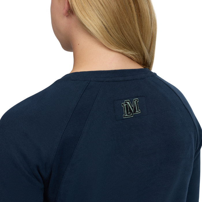 LeMieux AW26 Young Rider Shay Varsity Crew Varient Navy. Close-up back view of a woman wearing a navy crewneck sweatshirt, showing a small embroidered 'M' logo on the upper back.
