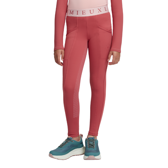 LeMieux AW26 Mini Pull Ons Varient Spiced Earth. A model wearing a pair of high-waisted, long-sleeve athletic leggings in a dusty rose pink color, paired with teal sneakers. The leggings feature a textured vertical panel on the lower leg and a wide waistband with the brand name 'LeMieux' printed in pink.