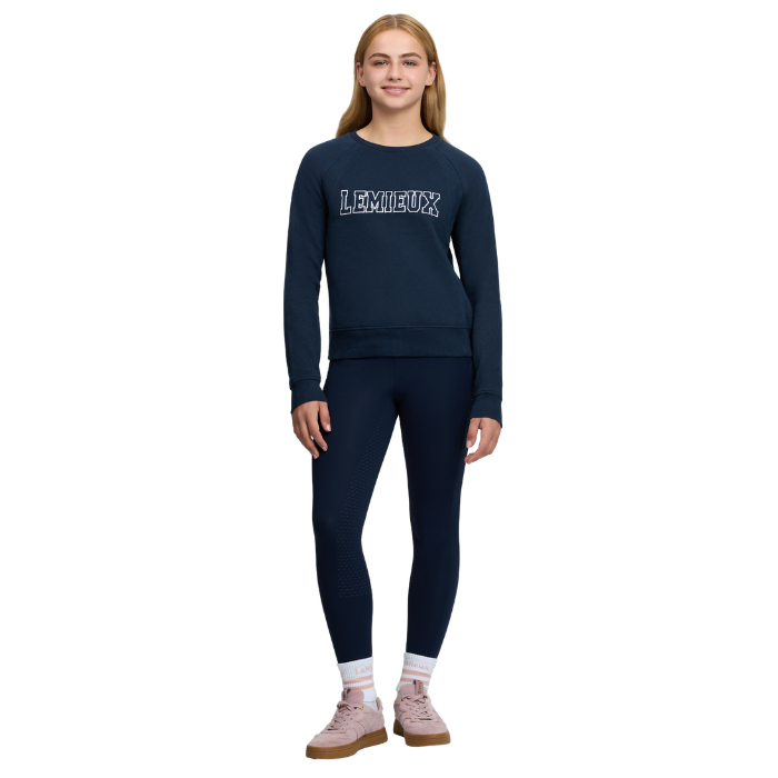 LeMieux AW26 Young Rider Shay Varsity Crew Varient Navy. A young woman modeling a navy blue sweatshirt and matching leggings set. The sweatshirt features the word 'LE MIEUX' printed across the chest in white with a dark outline.