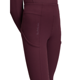 LeMieux AW26 Young Rider Orla Ribbed Pull Ons Varient Bramble. Close-up of a person wearing LeMieux ribbed riding tights in a deep burgundy color, showing the side pocket with the brand name printed vertically.