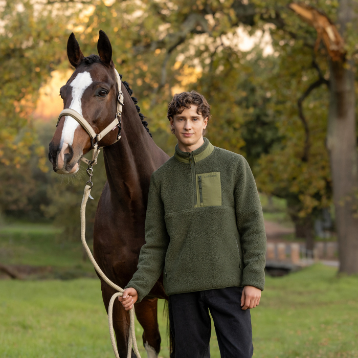 LeMieux AW26 Mens Borg Half Zip Sweat Varient Olive. Man wearing a green fleece stood with a horse in a woodland. 