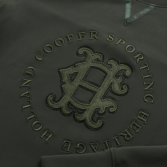 Holland Cooper Cranborne Crystal Crew Variant Ivy Green. Close-up of a dark olive green sweatshirt featuring an embroidered circular 'Holland Cooper Sporting Heritage' monogram logo on the chest.