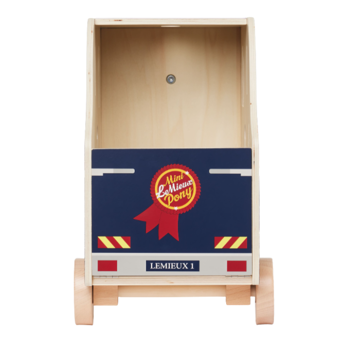 LeMieux AW26 Toy Pony Lorry Wooden Varient Brown. A wooden toy push box designed to look like a horse box, featuring a natural wood frame, light-colored wheels, and a navy blue front panel with a red ribbon badge and yellow accents.