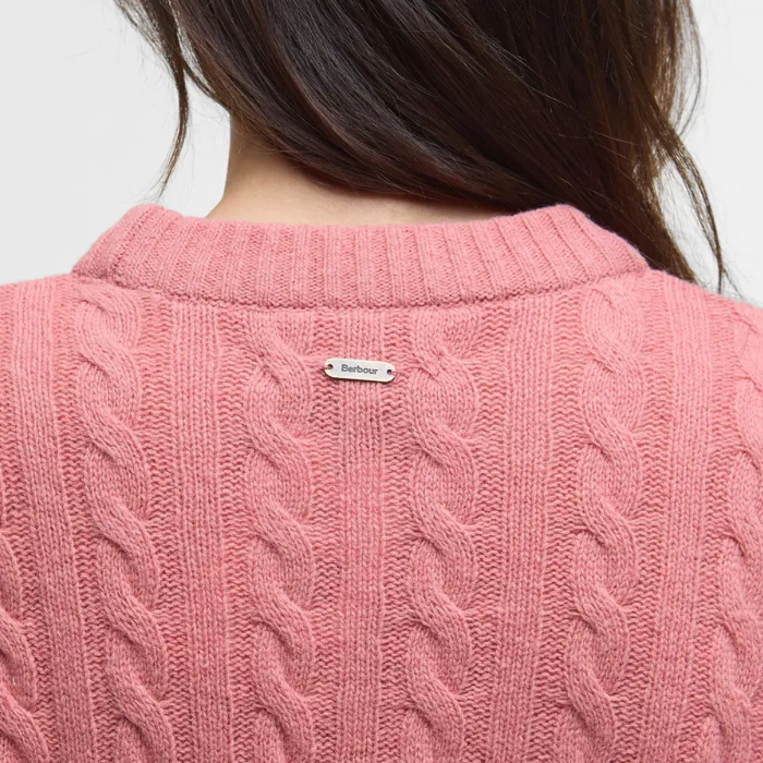 Close-up of a pink cable knit jumper with a 'Barbour' brand tag on a plain background
