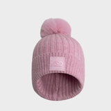 Pink knit beanie with logo and a pom-pom on a light grey background