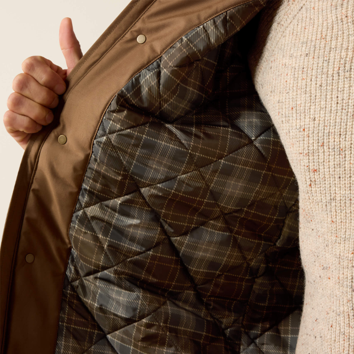 Close-up of a brown quilted jacket being opened by a person, showing a plaid pattern lining and a cream knit sweater.