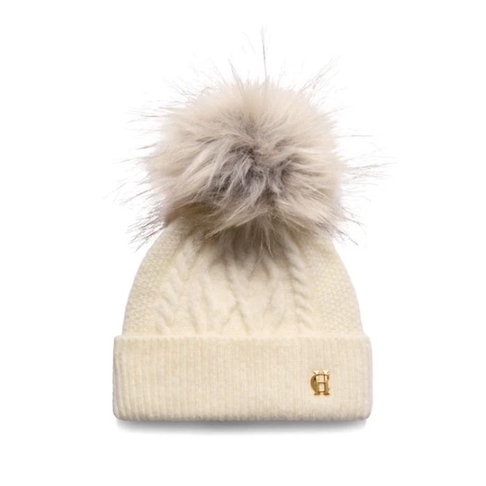 Holland Cooper Sloane Cable Bobble Hat Variant Cream. An off-white cable-knit beanie with a large beige faux-fur pom-pom and a small gold 'H' logo on the front cuff, shown against a plain white background.