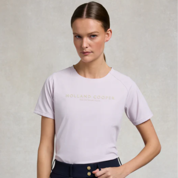 Holland Cooper Chiltern Crew Neck Tee Varient Dawn Pink. Woman wearing a light purple t-shirt with text on a plain background
