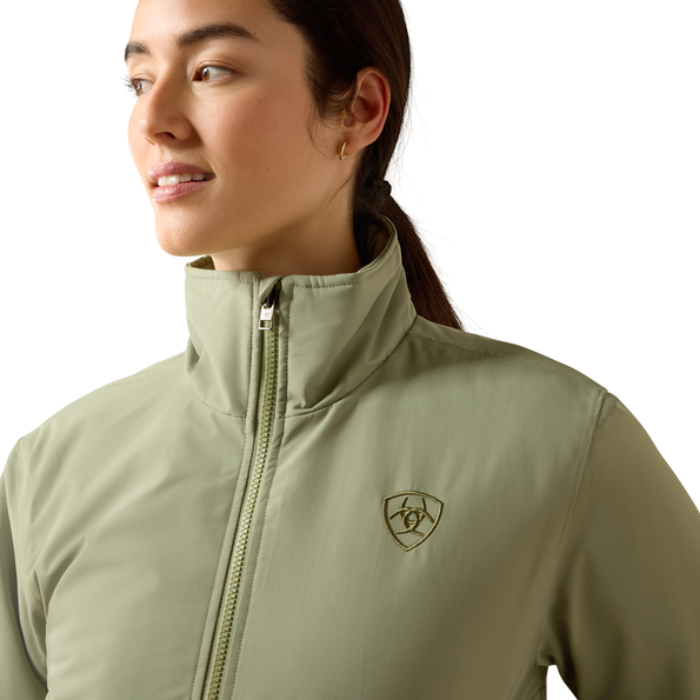 Ariat Women's Stable 2.0 Insulated Jacket Varient Oil Green. Woman wearing a olive bomber coat a with a high neck on a white background.