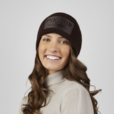 Pikeur Beanie Selection 285800 Variant Chocolate Brown. A smiling woman wearing a ribbed knit beanie in a brown color with a rectangular front patch reading 'PIKEUR'. 