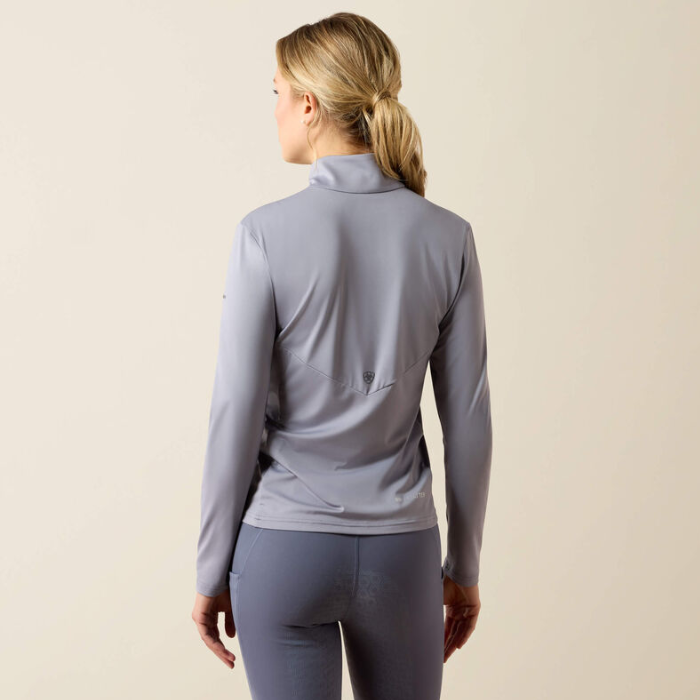 Ariat Ladies Lunaveil 1/2 Zip Long Sleeve Base Layer Variant QuickSilver. Woman wearing a silver/ blue base layer from behind against a beige background. 