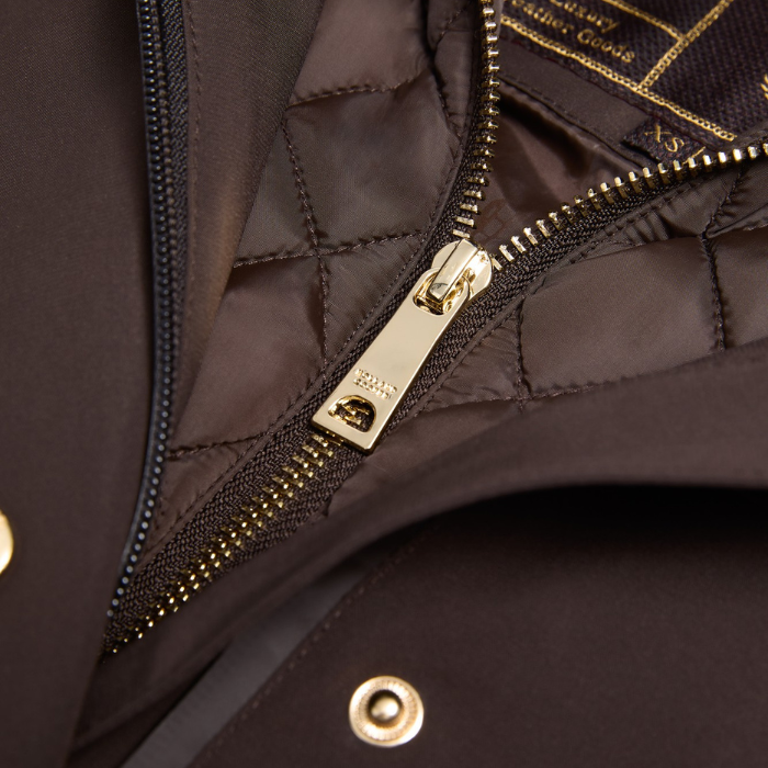 Holland Cooper Folgate Rain Coat Variant Chocolate. Close-up detail of a dark brown quilted jacket with a gold-tone metal zipper pull and gold branding text on the inner lining.