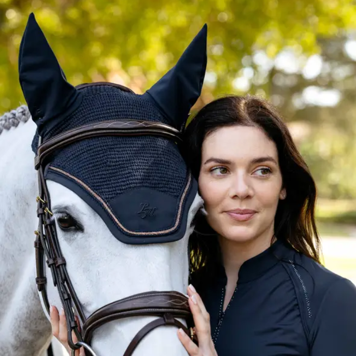 White horse wearing navy hood and bridle with person holding on faded background