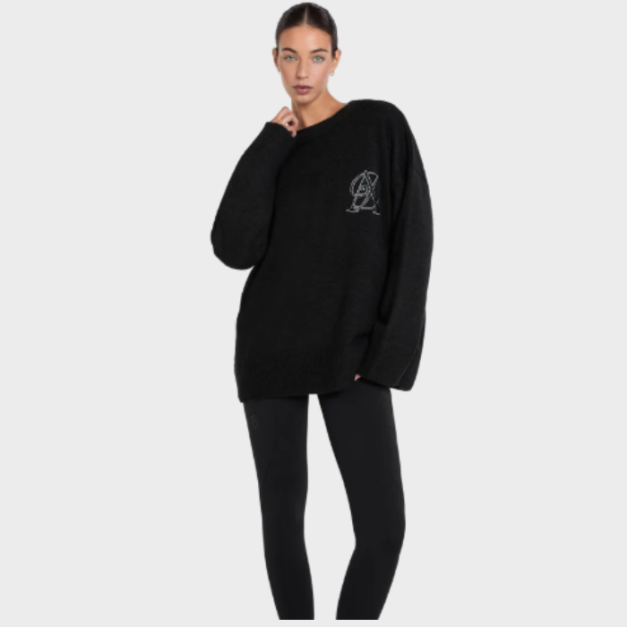 Person wearing a black oversized sweater with a logo on a light grey background