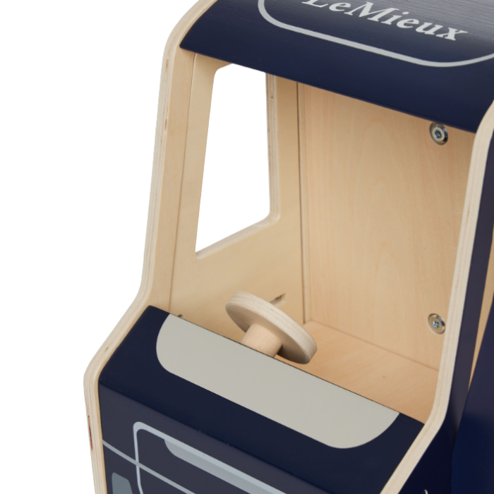LeMieux AW26 Toy Pony Lorry Wooden Varient Brown. Close-up of a wooden toy train cab with a dark navy blue exterior, natural light wood interior, and a small wooden steering wheel, on a white background. The brand name 'LeMieux' is visible on the top panel.