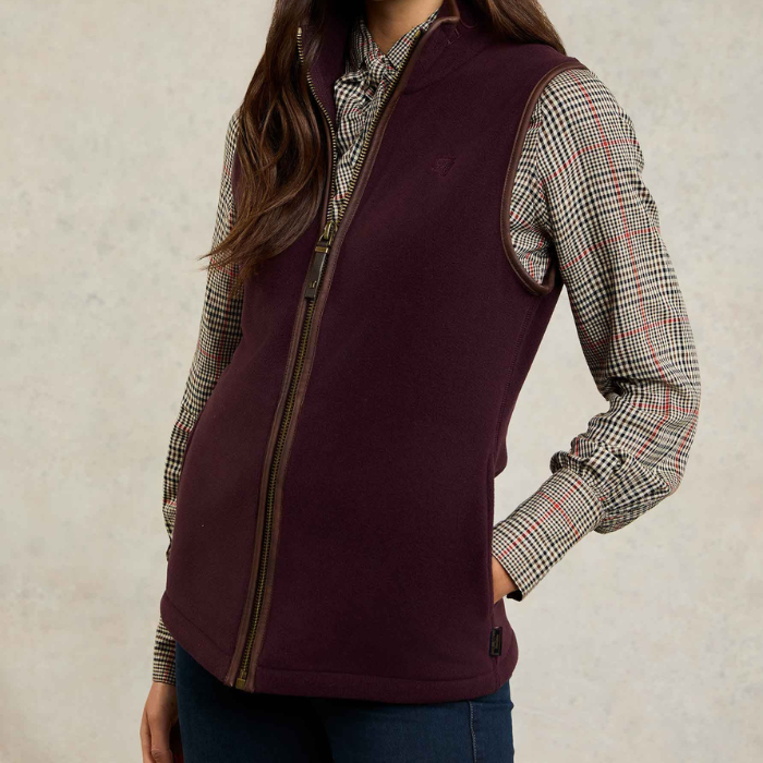 Holland Cooper Country Fleece Gilet Variant Mulberry. Mulberry gilet worn over a cheque shirt on a grey background. 