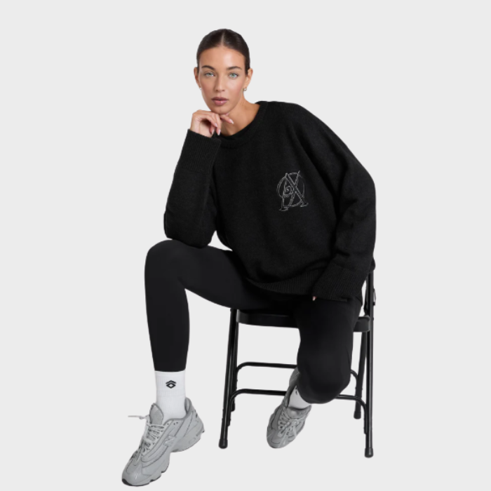 Person wearing a black sweatshirt with a logo, sitting on a chair against a white background