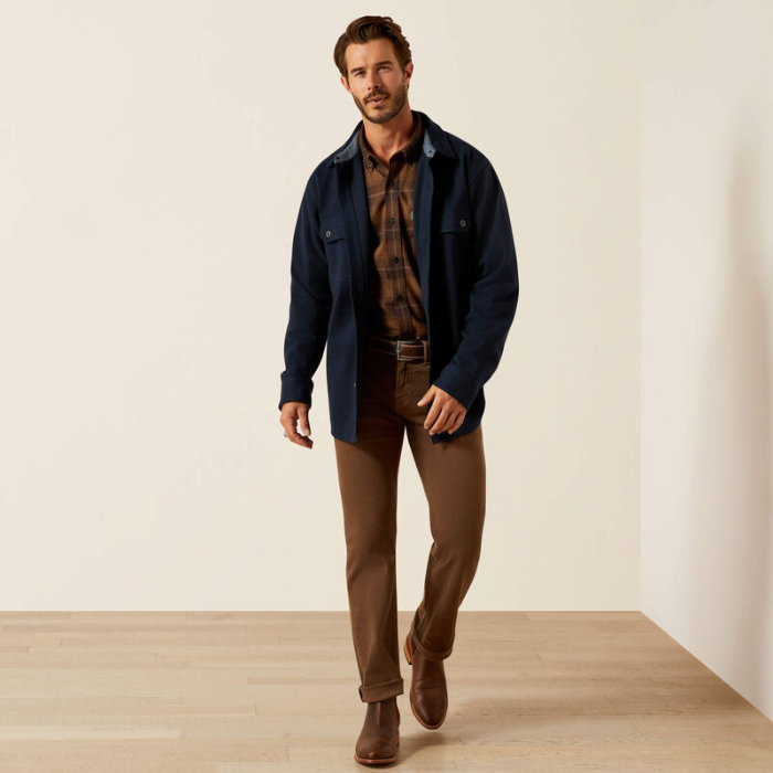 Man wearing a navy jacket, plaid shirt, and brown pants on a plain background