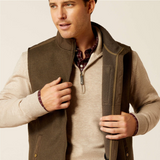 Man wearing a brown gilet over a beige sweater with a neutral background