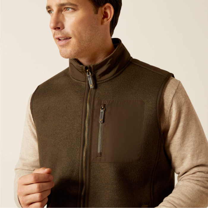 Man wearing a brown gilet over a beige shirt against a plain background
