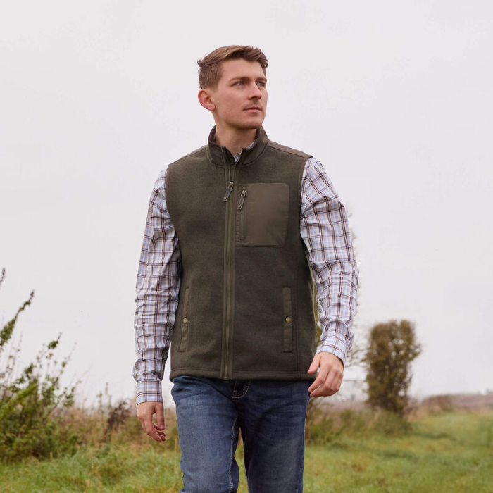 Man wearing a green gilet over a plaid shirt in an outdoor setting