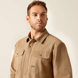Man wearing a beige shirt with a visible brand logo on a plain background