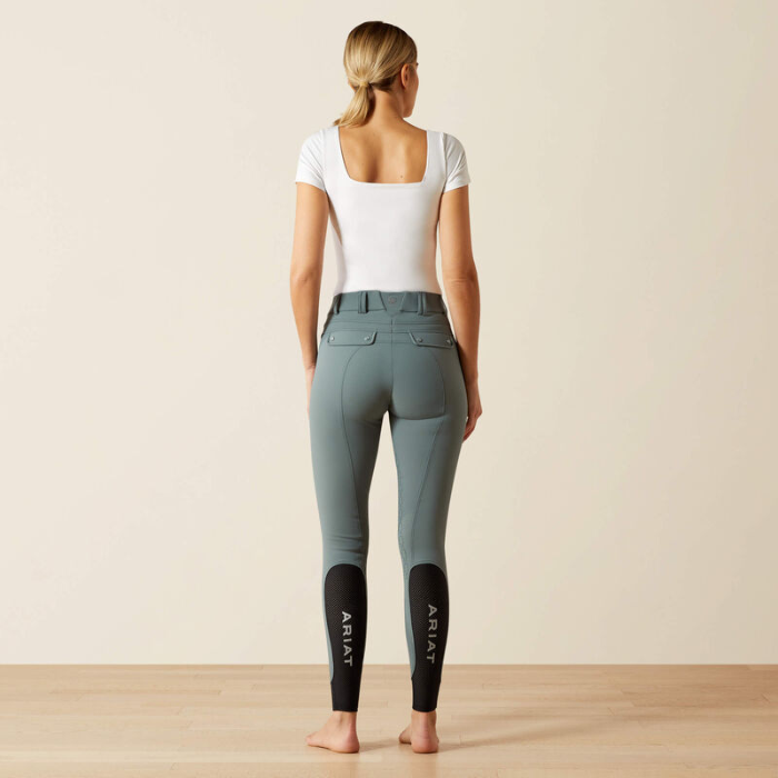 Person wearing green riding pants with 'ARIAT' branding on a plain background