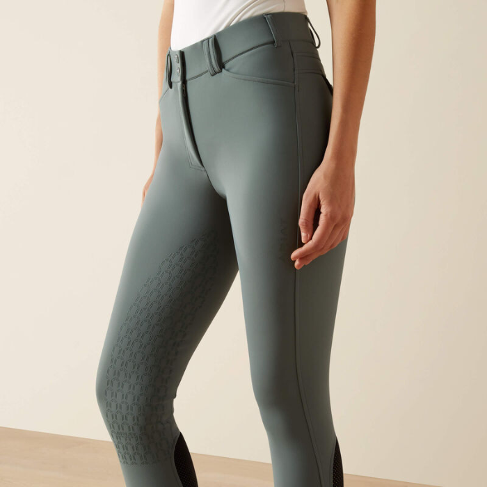 Green riding pants worn by a person on a beige background