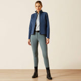 Woman wearing a blue jacket and grey riding leggings on a beige background