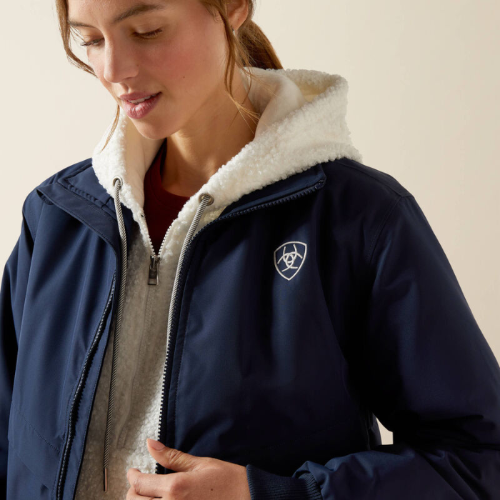 Woman wearing a navy blue jacket with a white logo on a beige background